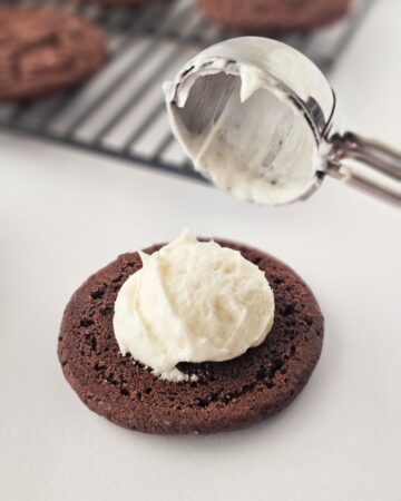 A chocolate cookie with a peppermint cream being placed in the middle. 