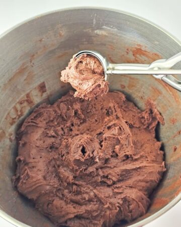 Chocolate cookie dough with a scoop pulling out a ball of dough. 