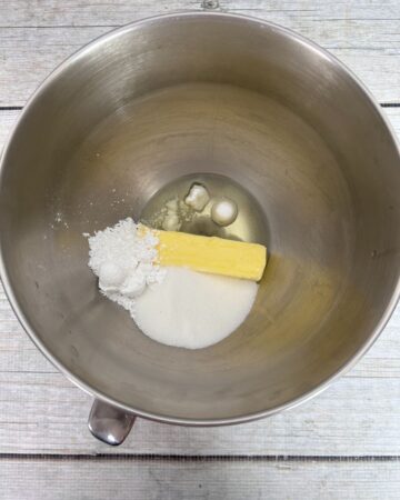 A stand mixer with butter, sugar, and confectioners sugar to make cookies.