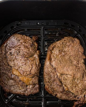 An air fryer basket with cooked rib eye steaks