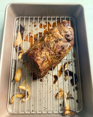 An eye round roast in a roasting pan with a rack under the roast.