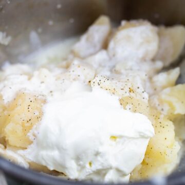 Cooked potatoes being made with sour cream, buttermilk, salt, and black pepper