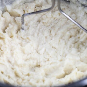 The vessel of an instant pot with potatoes being mashed with a potato masher.