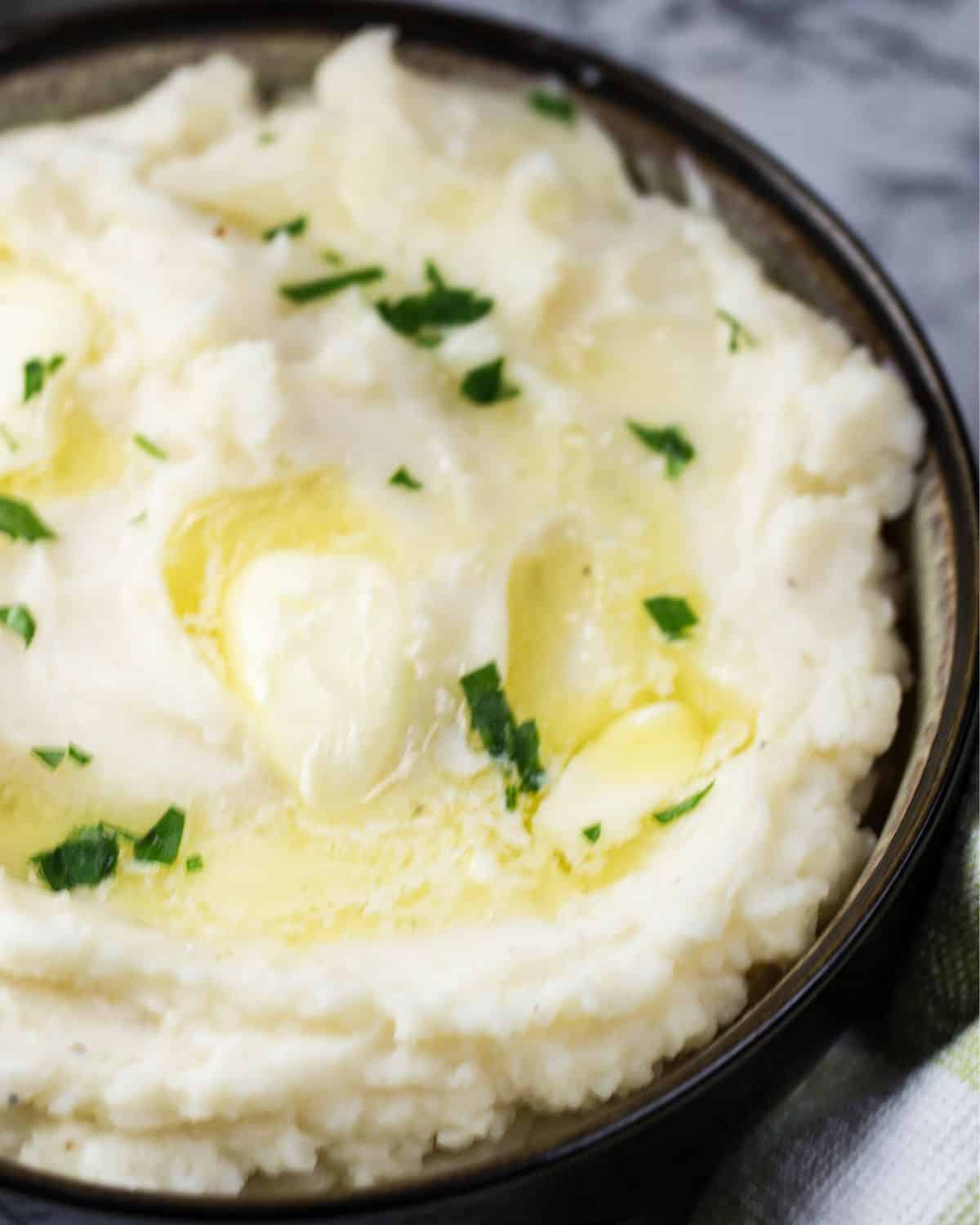 A bowl of mashed potatoes made in the Instant Pot with melting butter and chopped parsley on top.