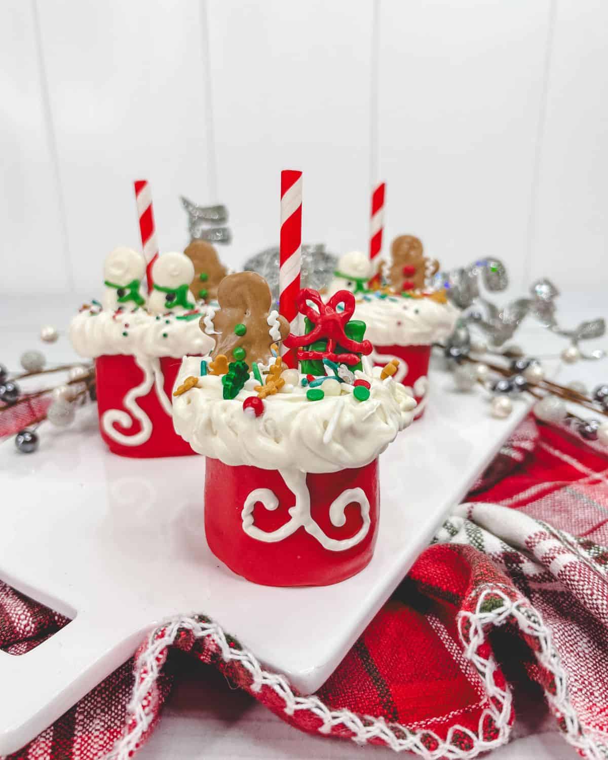 Santa marshmallow pops with sprinkles and a striped straw on a white board.