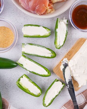 Jalapenos being stuffed to make smoked chicken thighs stuffed with jalapenos, cream cheese, wrapped in bacon.