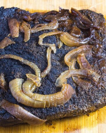 A coffee rub beef brisket that has been made in the slow cooker topped with sliced onions.