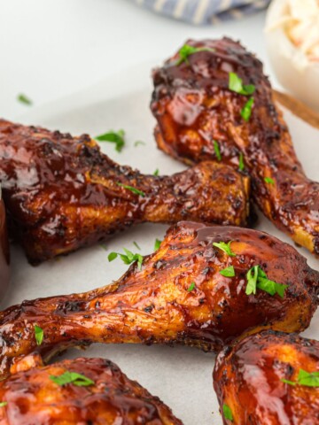 Air fryer bbq chicken drumsticks on a plate with BBQ sauce on the side.