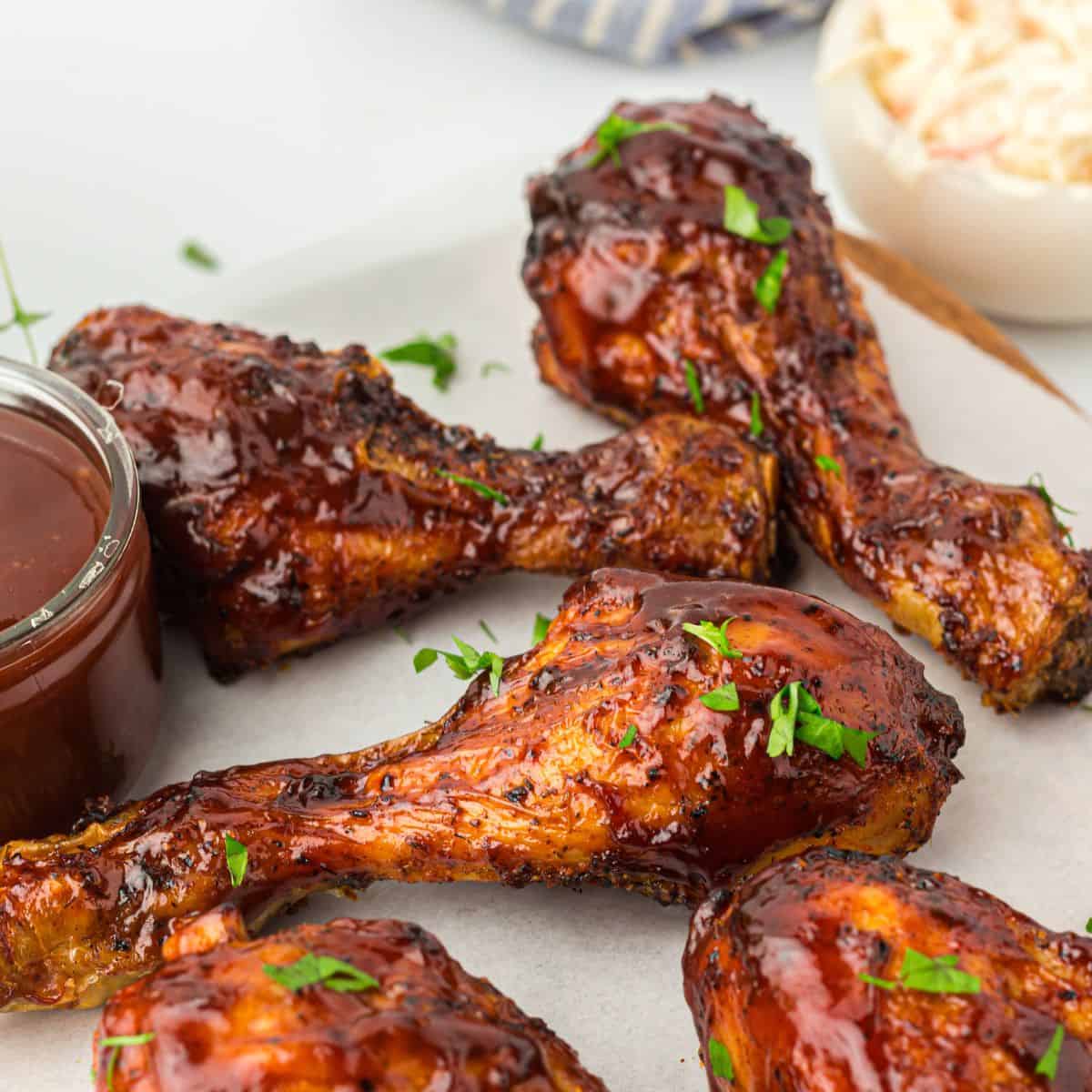 Air fryer bbq chicken drumsticks on a plate with BBQ sauce on the side.