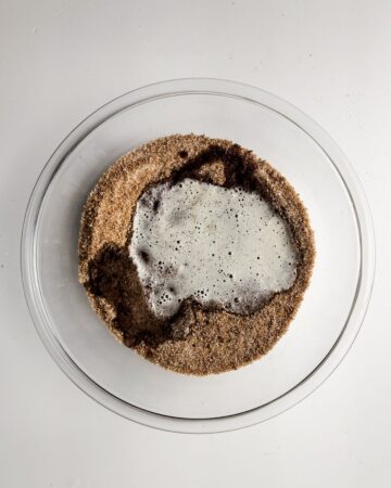 A glass bowl with sugar and brown butter to make browned butter pecan cookies.