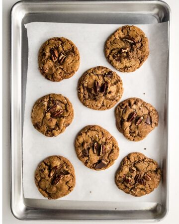 Brown butter pecan chocolate chip cookies with chopped pecans on top of the cookie on a baking tray.