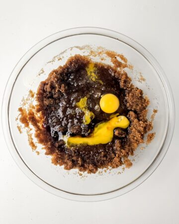 A glass bowl with brown sugar, white sugar, brown butter, and eggs to make a cookie batter.