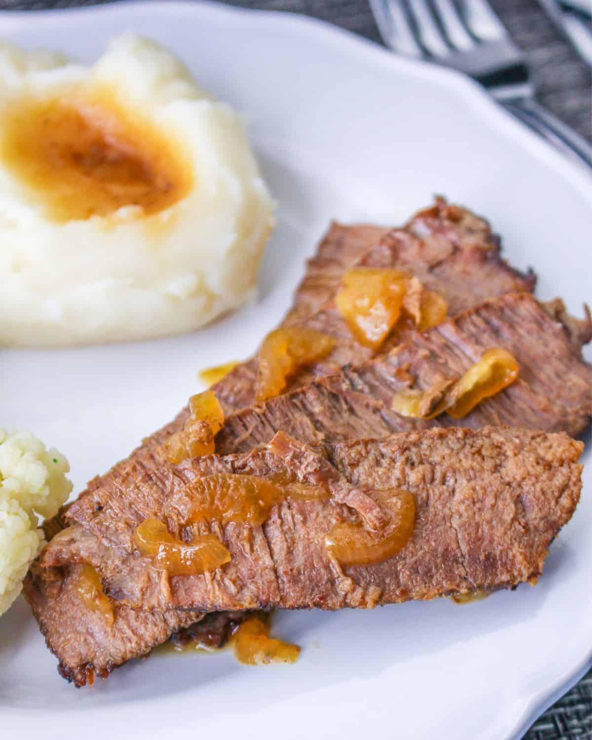 Sliced flank steak made in the slow cooker on a plate with mashed potatoes. 