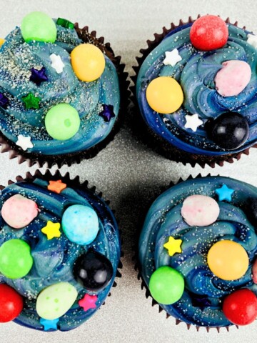 Chocolate cupcakes decorated with galaxy theme treats and a blue sky themed frosting.