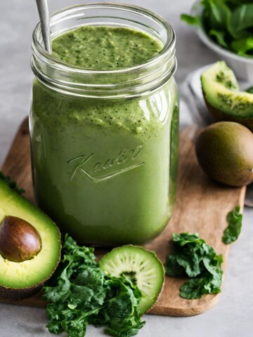 An easy green smoothie recipe on a wooden platter with fruit and veggies in front of the jar.