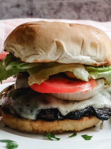 A grilled portobello mushroom burger topped with lettuce, tomato, and pickles on a bun.