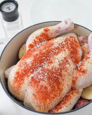A dutch oven with a whole chicken with seasonings and lemon on the chicken.