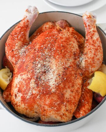 A seasoned whole roast chicken with lemon and potatoes in a Dutch oven.