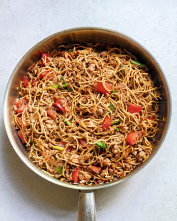 Teriyaki noodles with pork and vegetables in a saute pan.