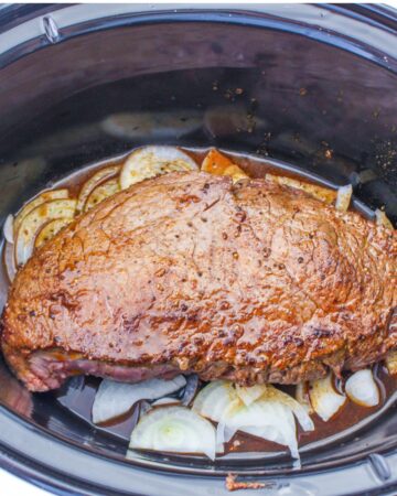 A flank steak that has been browned on top of sliced onions with red wine vinegar in the slow cooker.