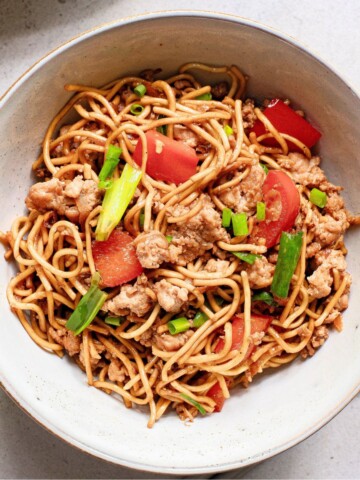 A bowl of Asian noodles with pork, peppers and green onions in a teriyaki sauce.