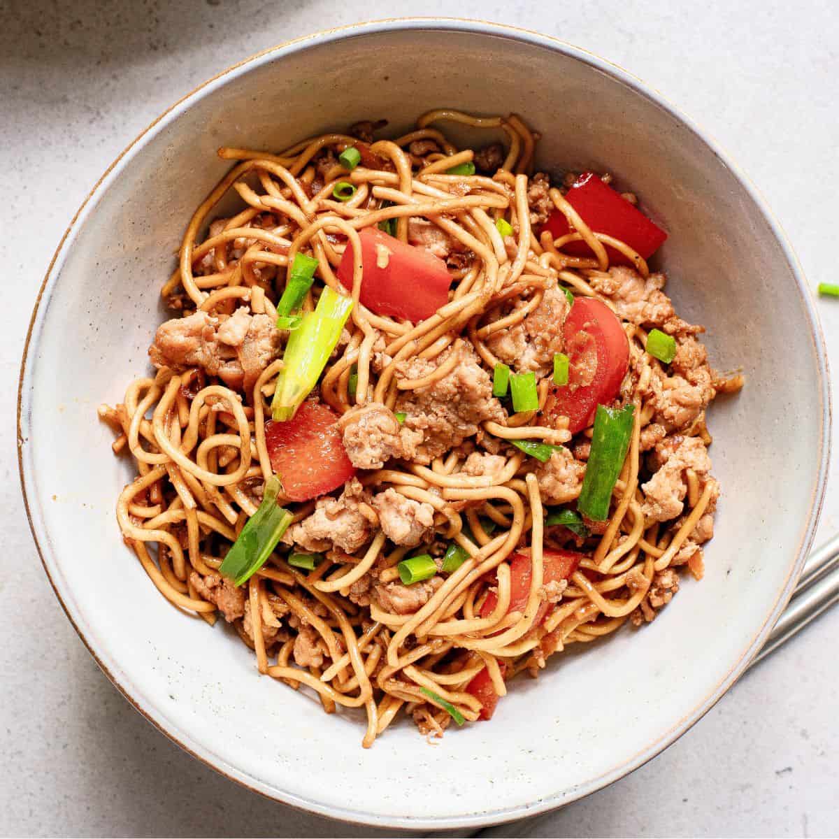 A bowl of Asian noodles with pork, peppers and green onions in a teriyaki sauce.