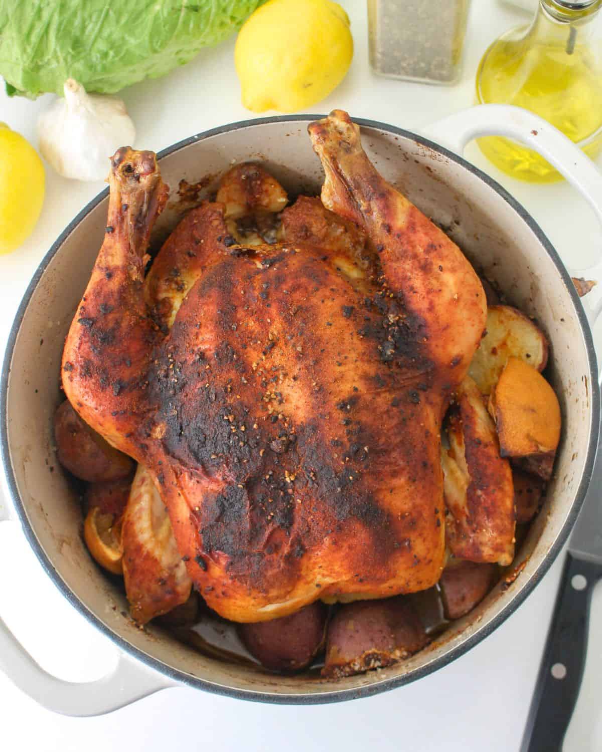A dutch oven with potatoes and roasted chicken with lemon and spices.