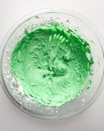 A large glass mixing bowl with whipped cream cheese mixed with green food gel for a grasshopper pie. 