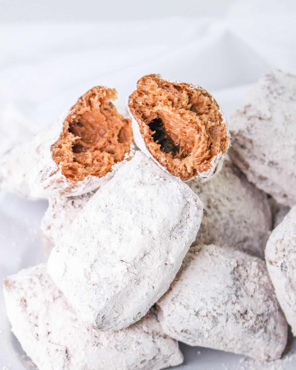 Chocolate beignets with powder sugar sliced in half to see the chocolate interior.