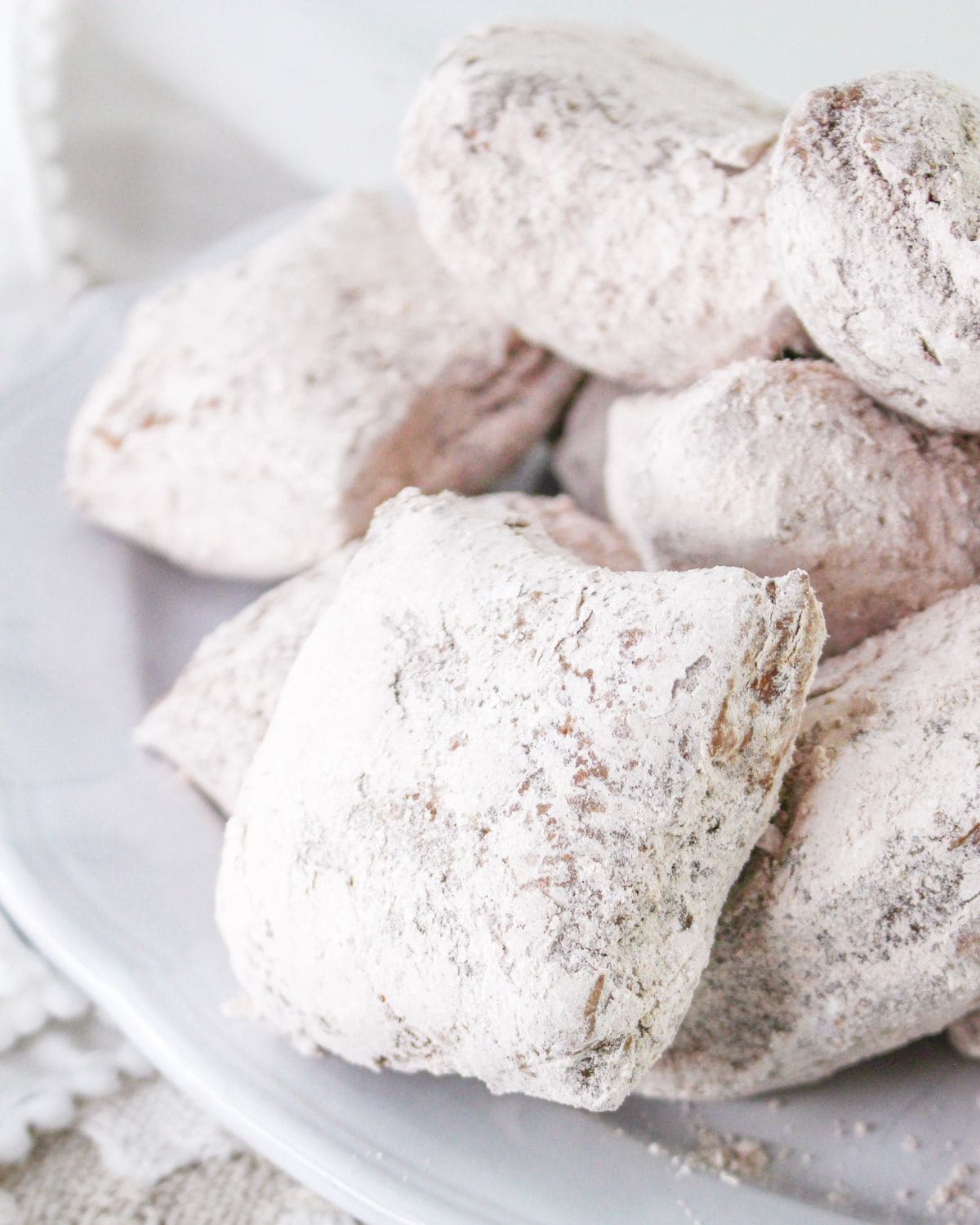 Chocolate flavored beignets on a plate covered with confectioners sugar.