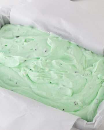 A loaf pan with a slice of parchment paper filled with homemade ice cream.