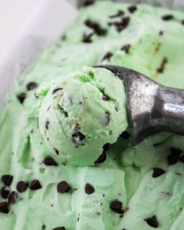 Homemade grasshopper ice cream with chocolate chips being scooped up with a metal ice cream scooper.