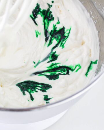 A large mixing bowl with whipped cream being infused with green food coloring and sweetened condensed milk to make grasshopper ice cream.