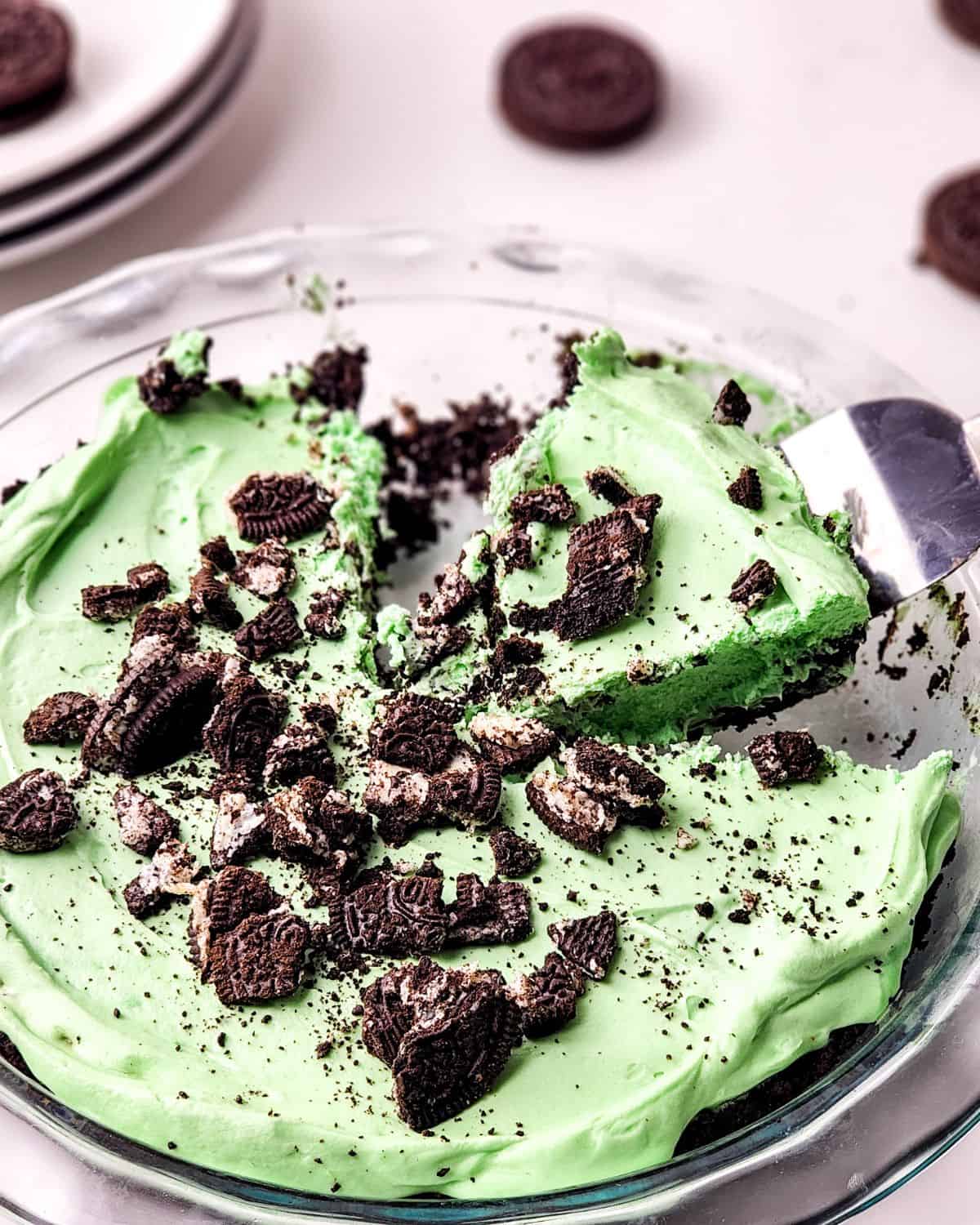 A pie plate with grasshopper pie in an Oreo crust in a pie pan. There is a slice of pie being picked up out of the plate. 