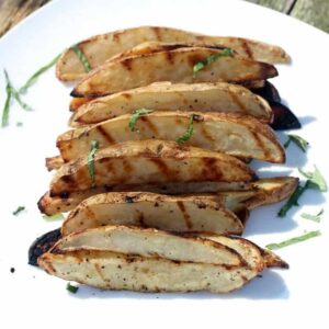 Grilled potato slices on a plate with seasoning and shredded basil.