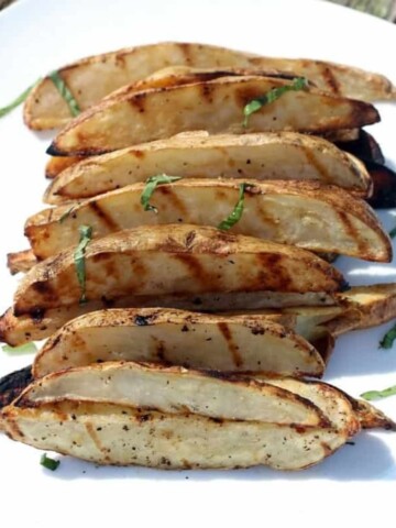 Grilled potato slices on a plate with seasoning and shredded basil.