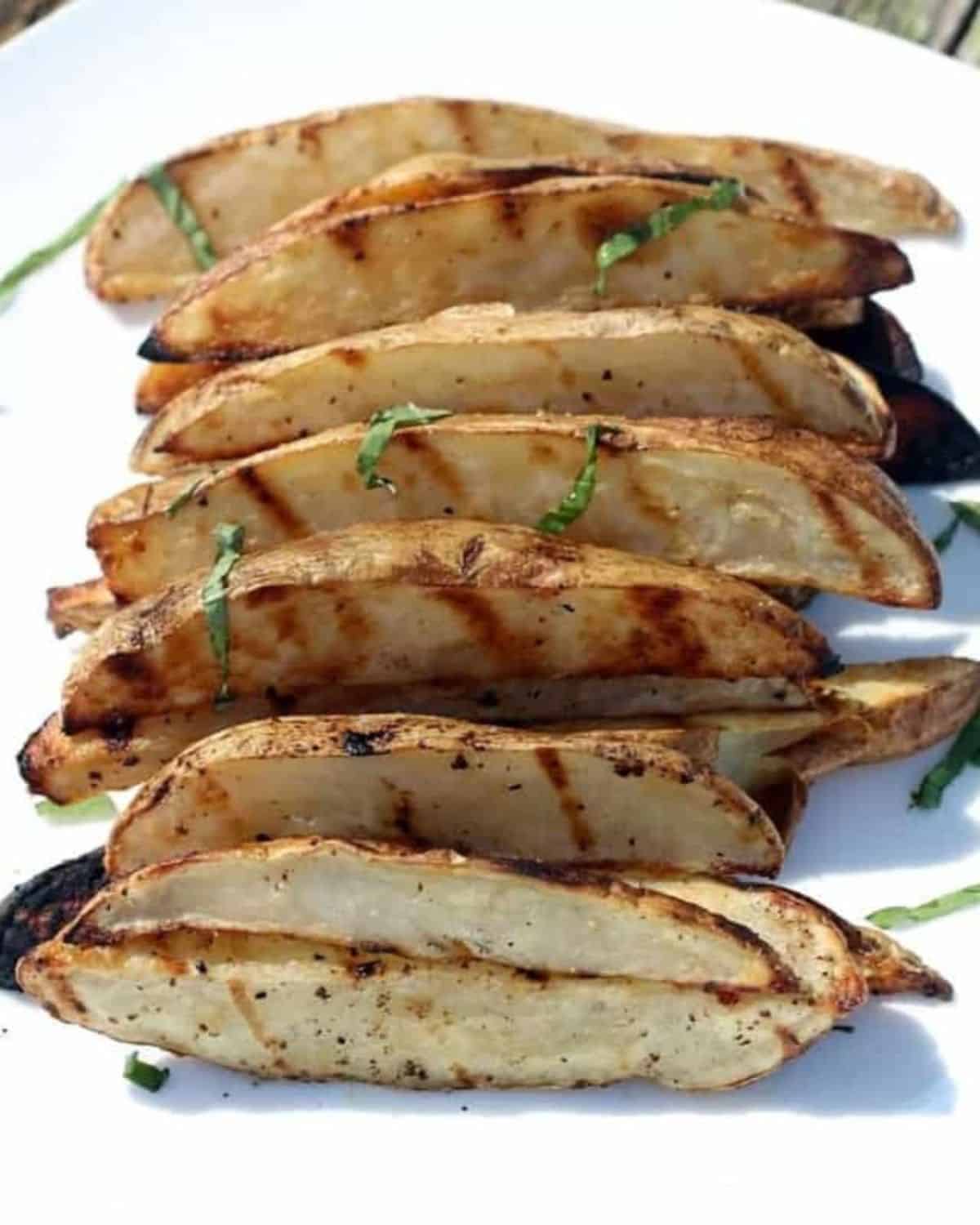 A white plate with sliced potato wedges that have been grilled.