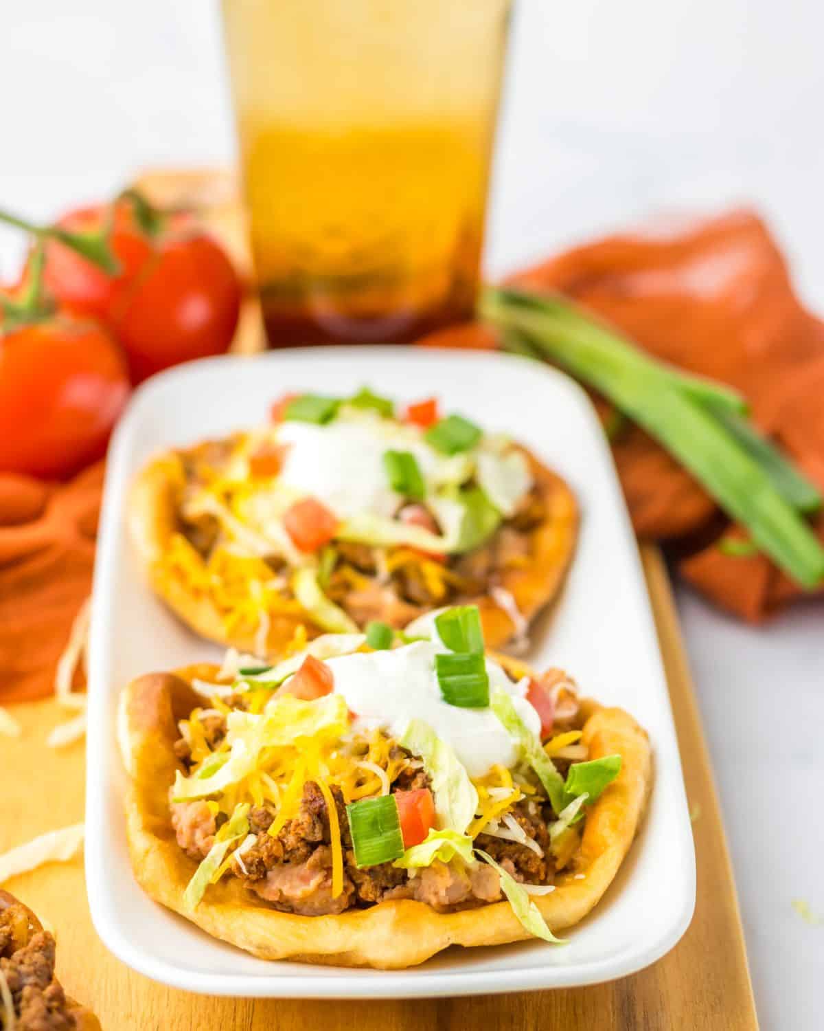 Fry bread tacos on a plate topped with taco meat, lettuce, shredded cheese and sour cream.