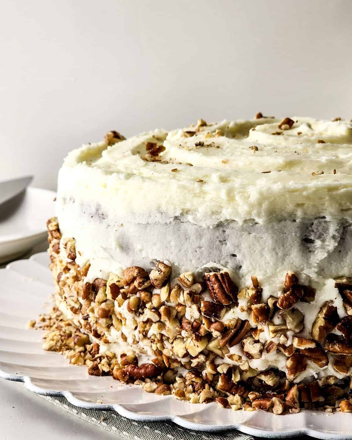 A carrot cake with cream cheese frosting and chopped pecans on the side of the cake.