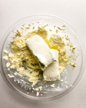 Cream cheese frosting being made in a glass bowl with whipped butter and cream cheese.