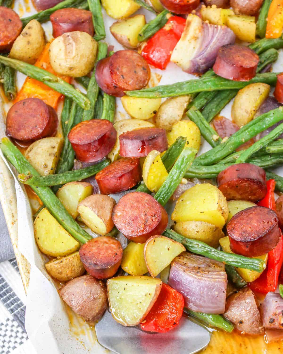 Andouille sausage, potatoes, and string beans on a sheet pan for a sausage dinner.