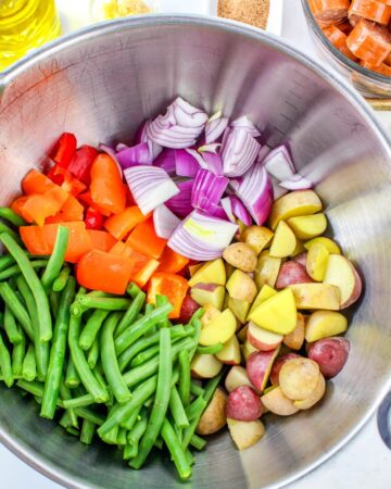 Ingredients to make cajun sheet pan sausage and potatoes in a large mixing bowl.