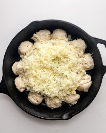 A cast iron skillet with pizza dough balls around the sides and a dip in the center for a pizza dip.