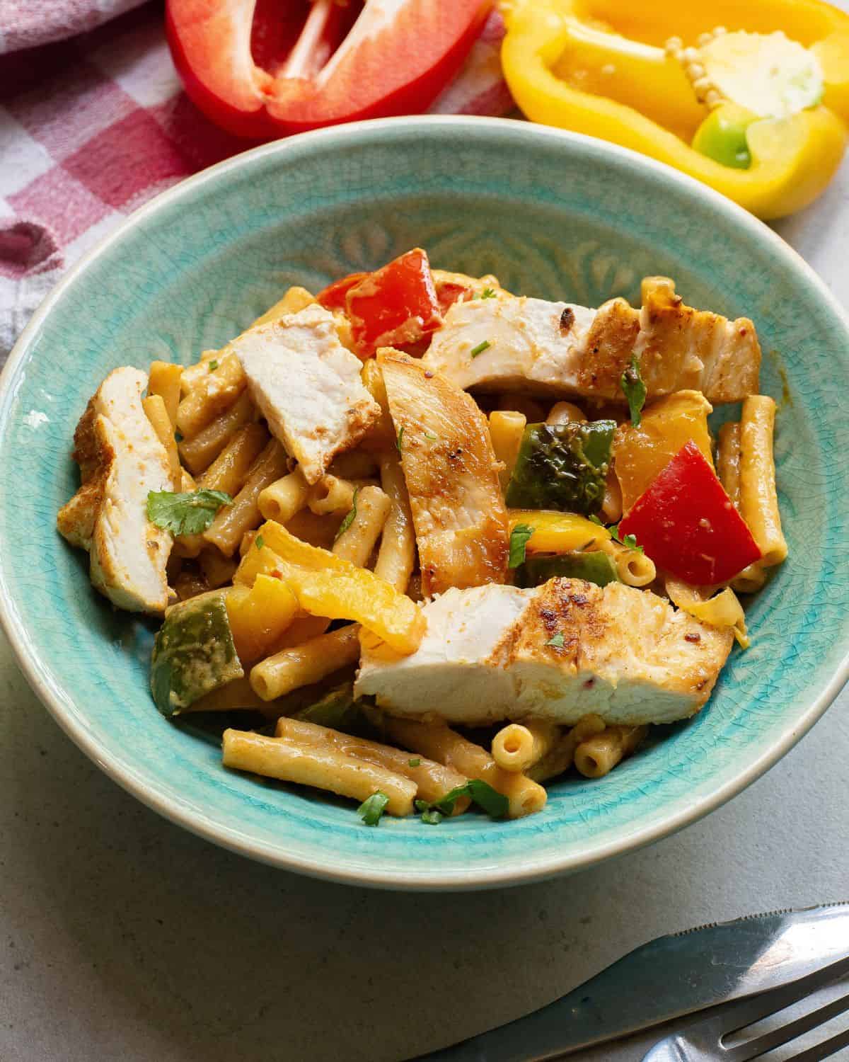 A bowl of chicken fajita pasta with sliced cooked chicken and peppers over pasta.