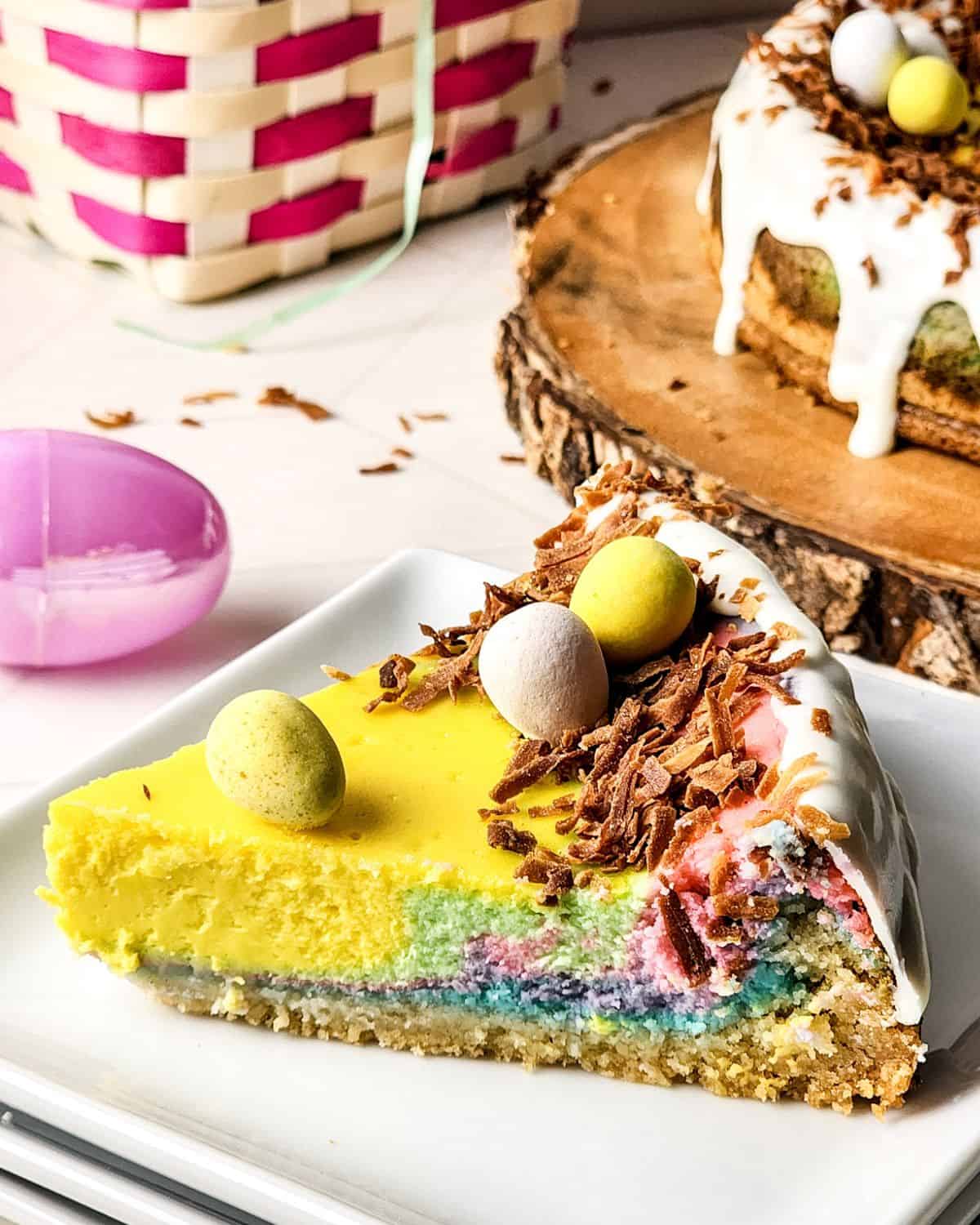 A slice of Easter egg cake with rainbow cake, shaved chocolate, and easter chocolate eggs on top of the cake.