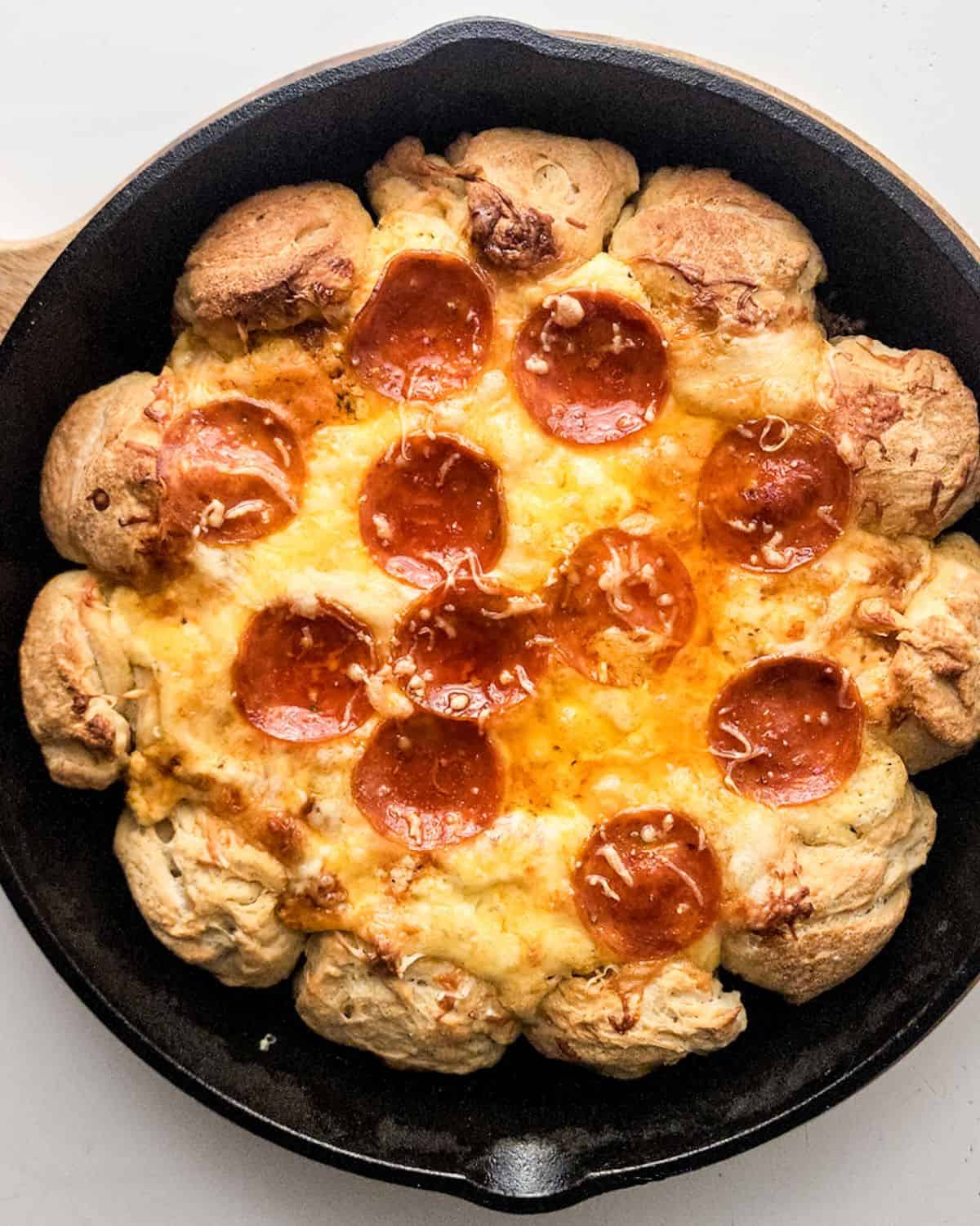 Pizza dip made in a cast iron skillet with garlic butter pizza dough balls around the sides.