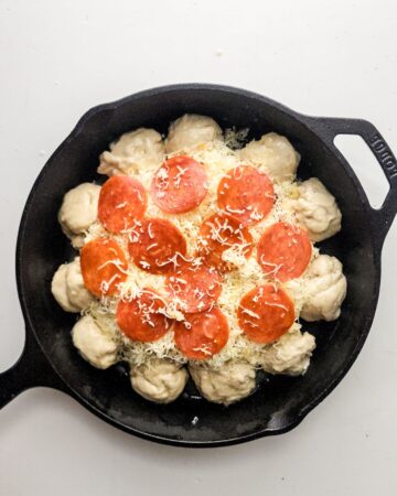 A cast iron skillet with pizza balls and a dip in the center to make pizza dip.