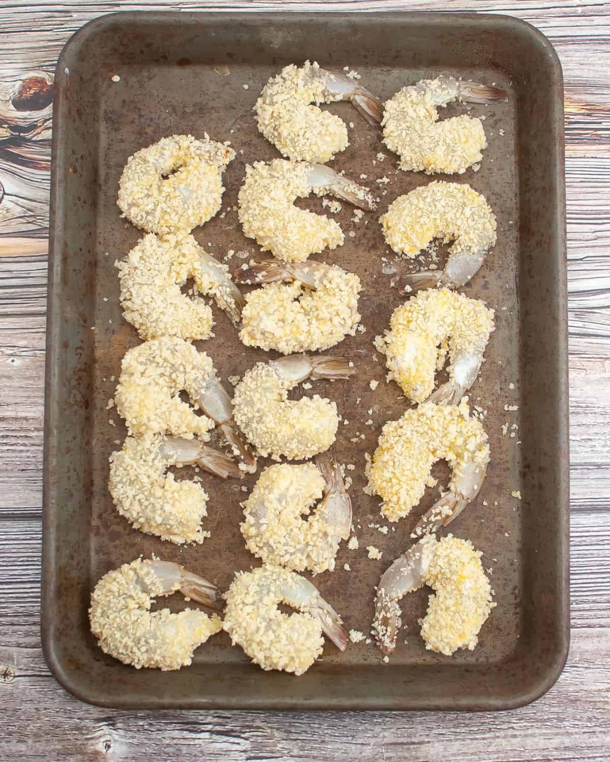 Shrimp in Panko breading on a pan waiting to be fried.