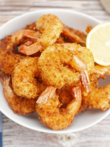 Fried shrimp with panko bread crumbs in a bowl with lemon wedge.