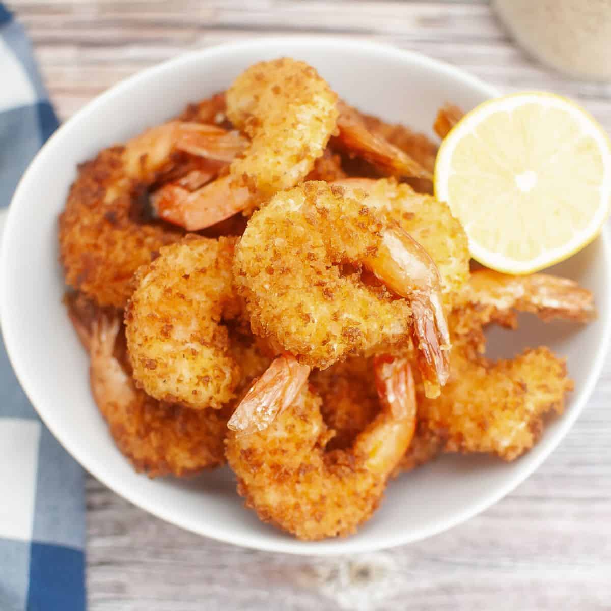 Fried shrimp with panko bread crumbs in a bowl with lemon wedge.